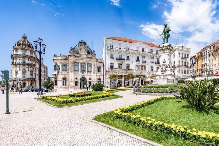 Vibrant scene of Coimbra's Praça 8 de Maio, featuring iconic architecture and lush gardens under a clear sky.