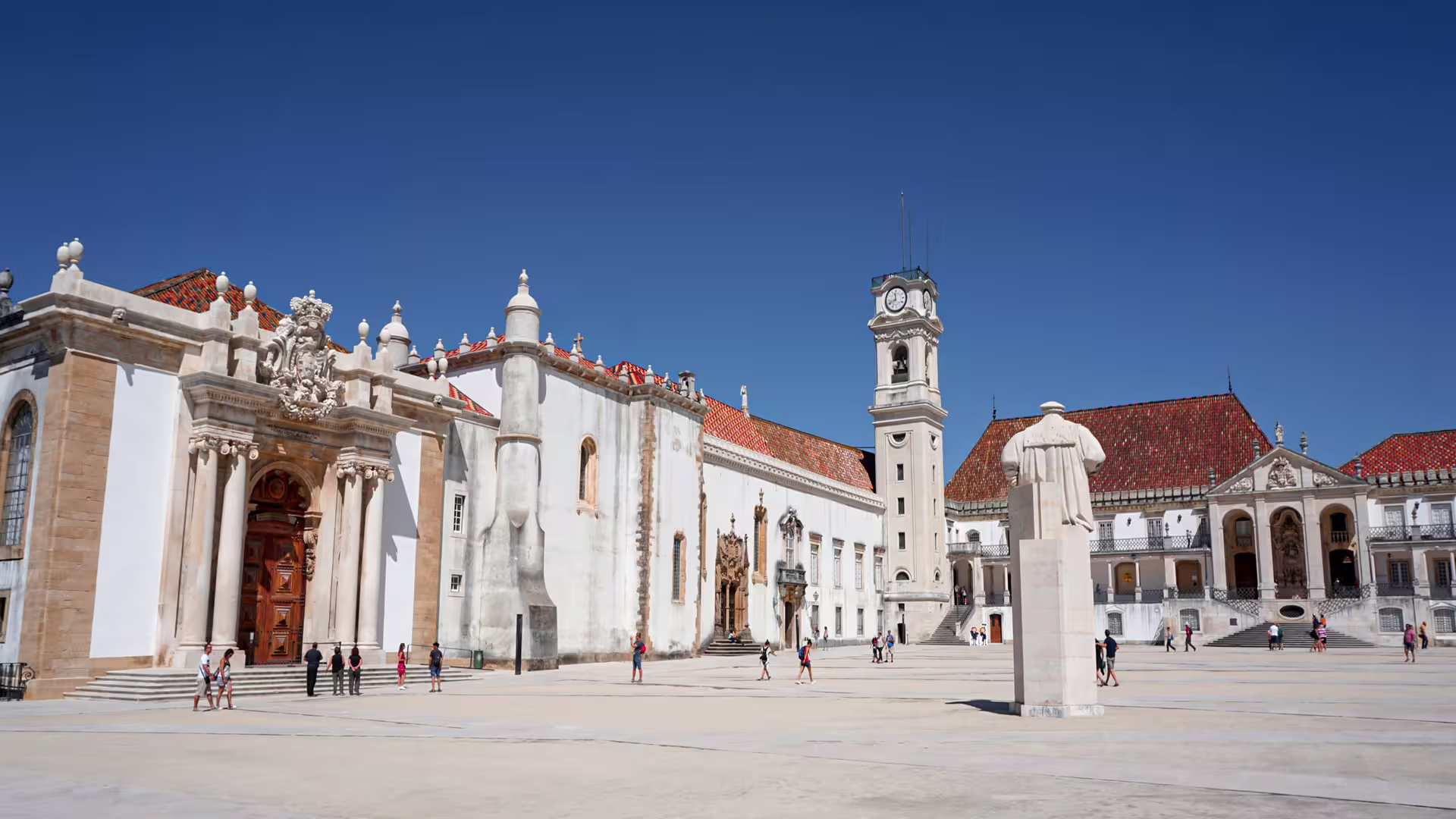 Historic University of Coimbra courtyard with ornate architecture and clock tower under a clear blue sky, ideal for private tours.
