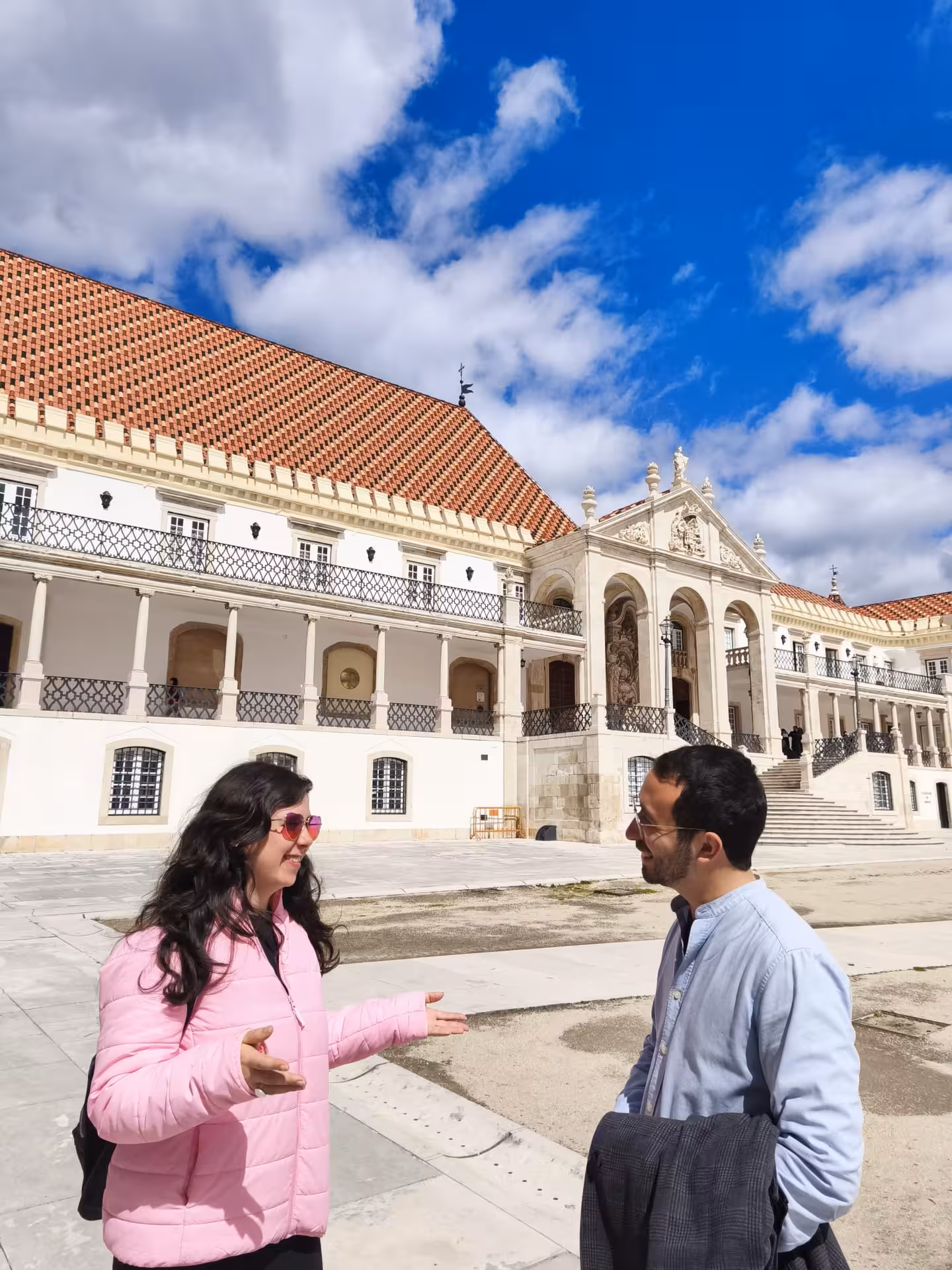 Tourists enjoying a sunny day at the historic courtyard of Coimbra University, showcasing its stunning architecture.