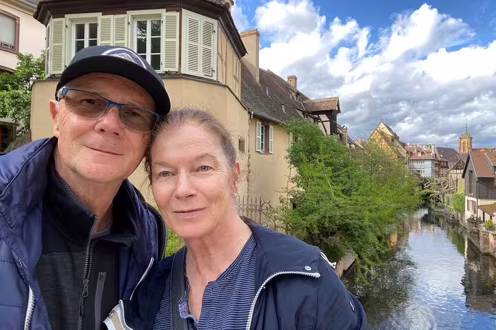 Couple selfie along Colmar Little Venice canal with half-timbered houses on a self-guided walking tour