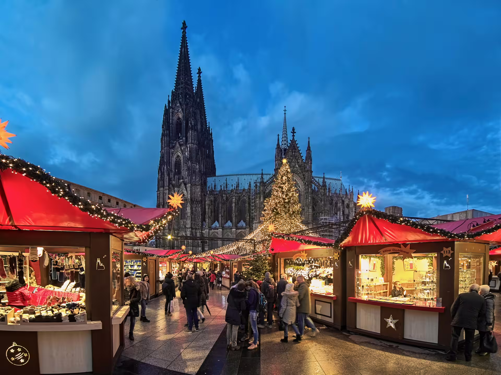 Cologne Cathedral Christmas market at dusk, festive stalls and lights on a 1-day walking tour audioguide