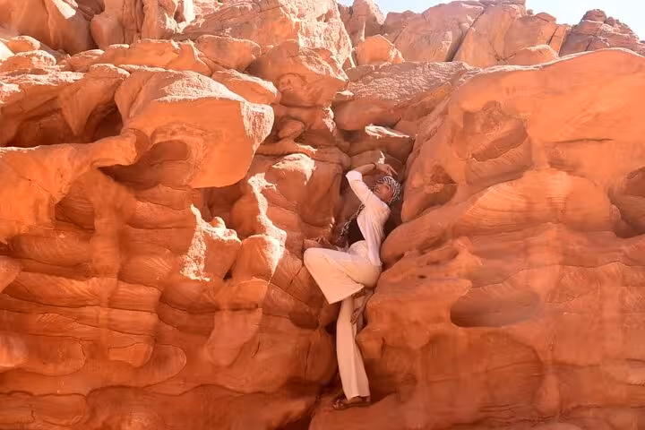 Traveler climbing red sandstone walls in Colored Canyon on Sharm El Sheikh jeep safari to Blue Hole Dahab