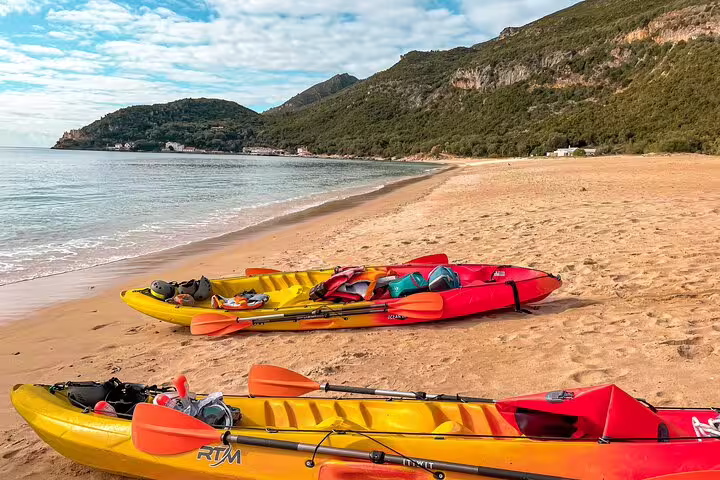 Colorful kayaks with gear on a sandy beach, ready for a full-day adventure tour departing from Lisbon.