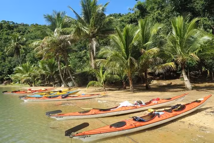 Colorful kayaks lined up on a sandy beach with palm trees, ready for a Paraty coastal adventure.