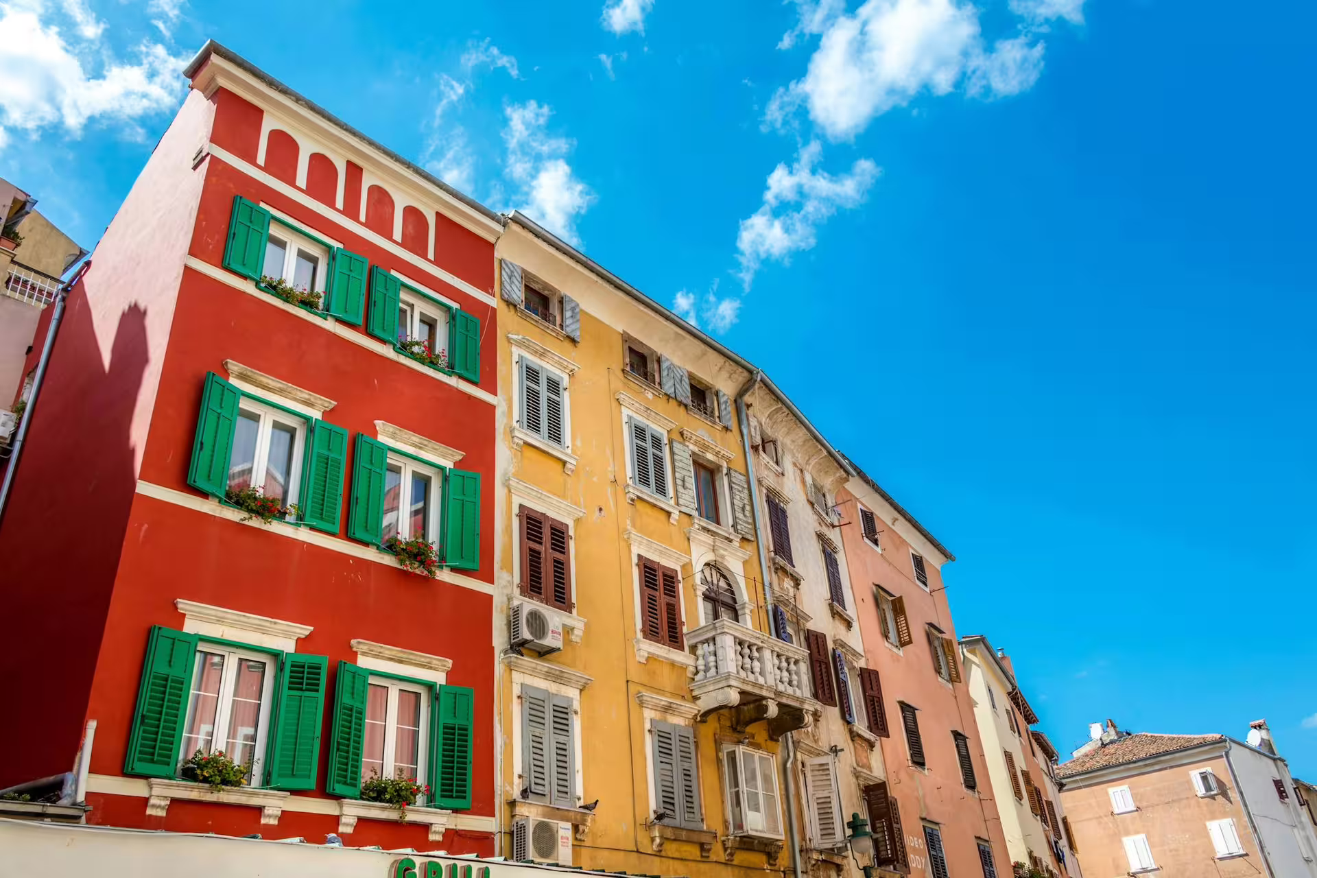 Colorful Rovinj buildings with green shutters under blue sky, photographed on the Ancient Istria tour from Pula