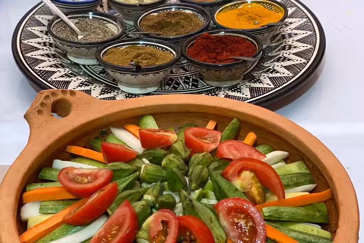 Colorful vegetable platter with fresh tomatoes and cucumbers beside a variety of spices, ideal for a culinary class setting.