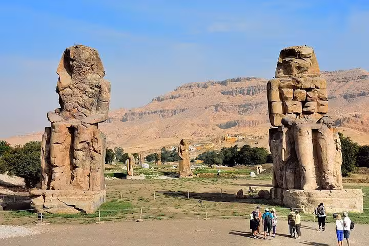 Colossal statues of Memnon stand tall in the desert landscape of Luxor, drawing visitors on guided historical tours.