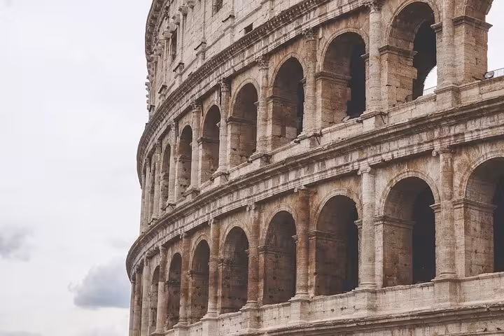 Close-up of the Colosseum's ancient arches against a cloudy sky, highlighting Rome's iconic architecture.
