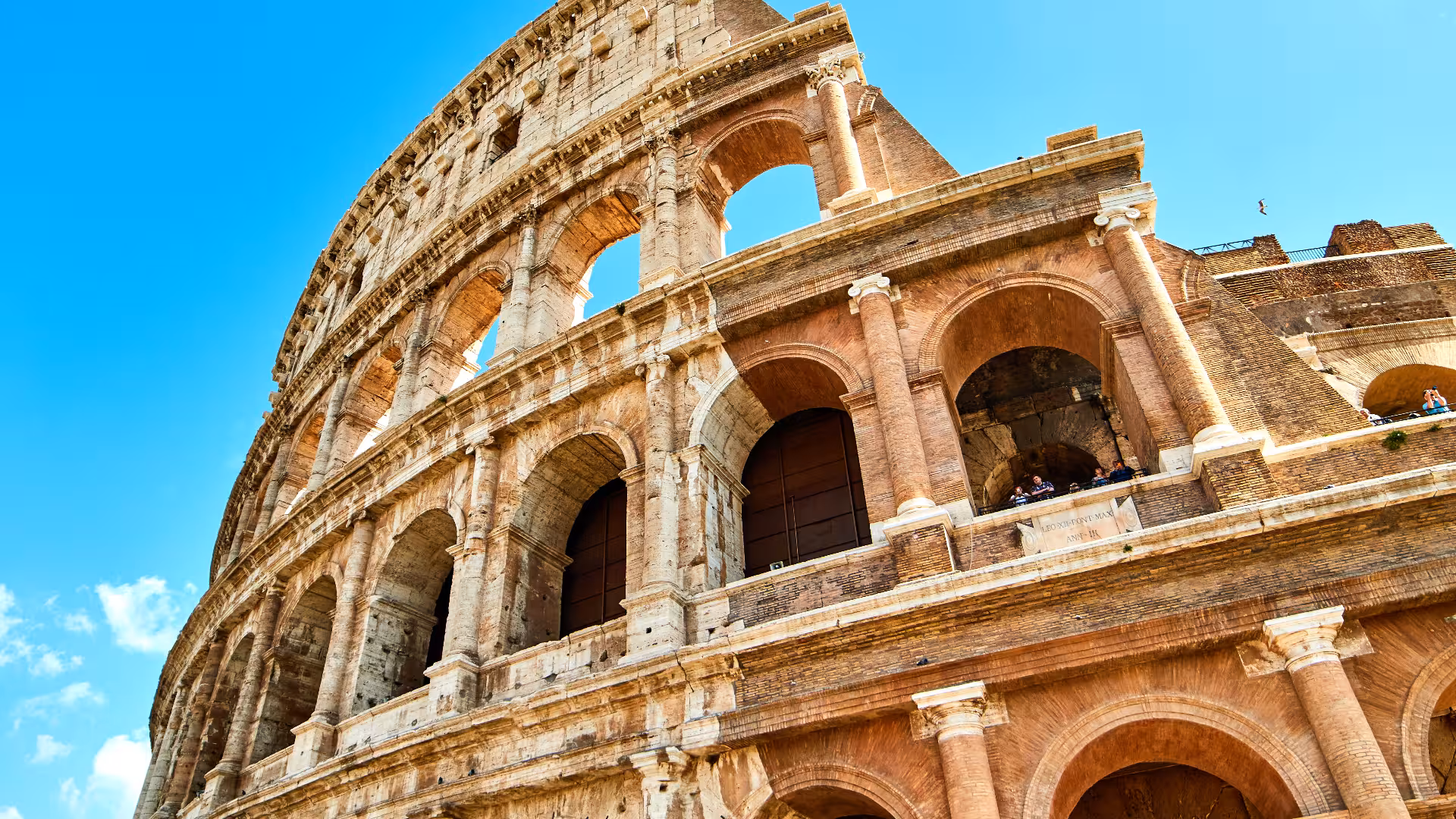 Close-up of the Colosseum's ancient arches in Rome under a bright blue sky, perfect for a historical exploration tour.