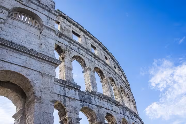 Colosseum's majestic arches under a bright blue sky, showcasing Rome's historical grandeur and elegance.