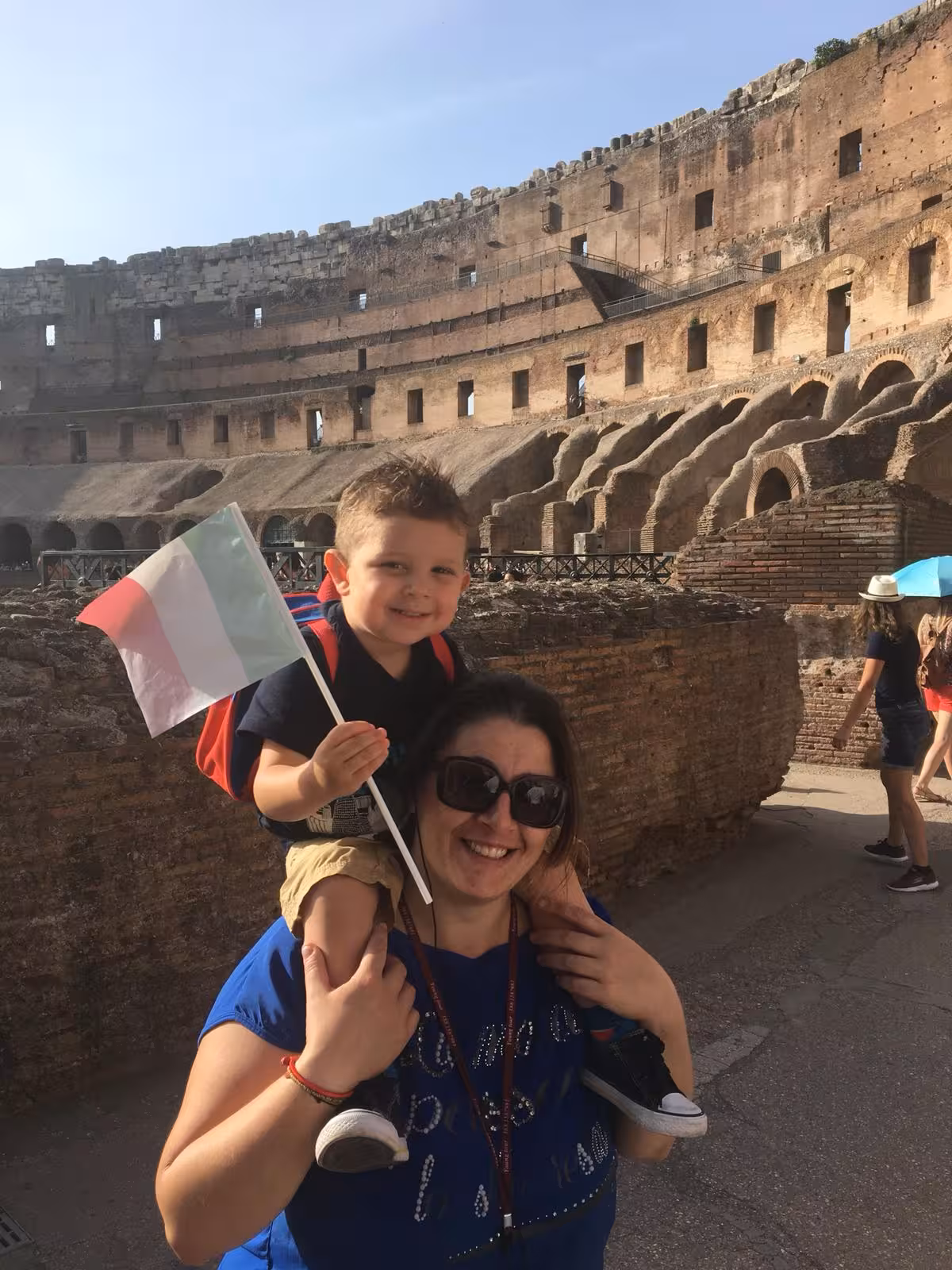 Smiling woman with child holding an Italian flag inside the Colosseum, highlighting family-friendly tour aspects.