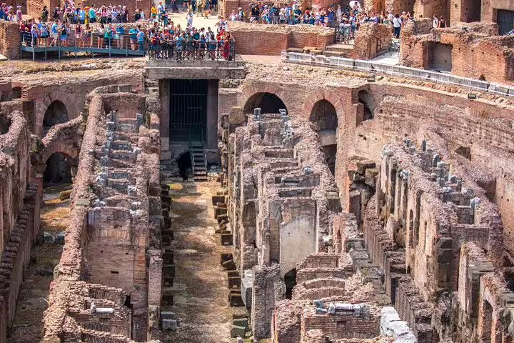 Guided tour guests viewing the underground hypogeum and gladiator passages from the Colosseum arena floor