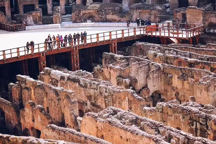 Small group walking along the reconstructed arena floor bridge above the Colosseum hypogeum on a guided gladiator tour