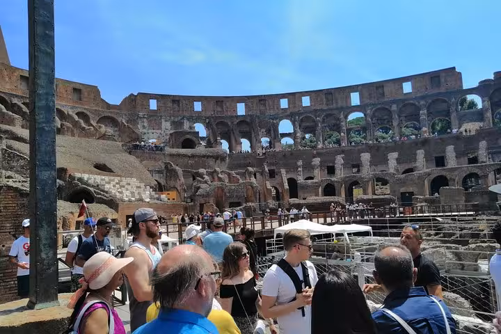 Tourists exploring the historic Colosseum interior under a bright blue sky during a guided tour in Rome.