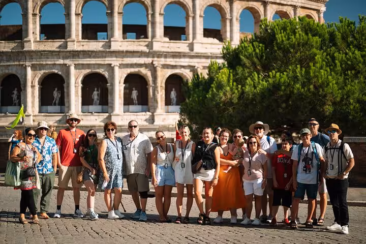Group of tourists enjoying a guided tour in front of the iconic Colosseum, Rome's ancient amphitheater, under a clear blue sky.