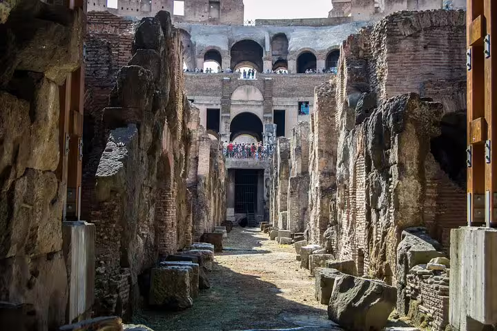 View along the Colosseum hypogeum with ruined walls and visitors above, part of official guided tour with Palatine Hill