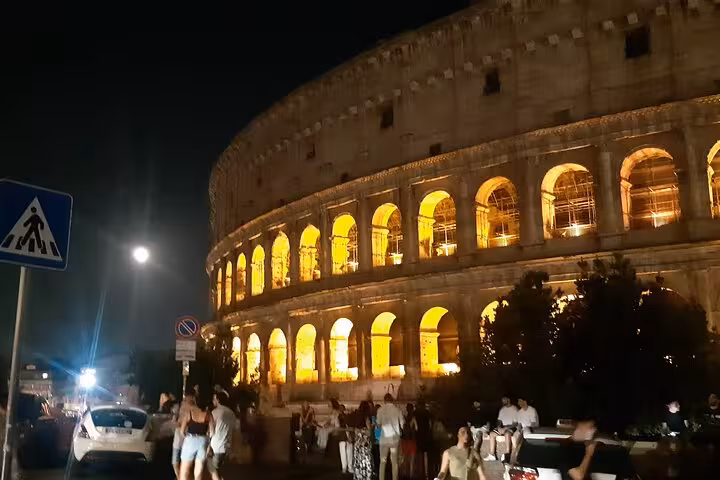 The Colosseum illuminated at night with visitors exploring, capturing the essence of a Rome evening tour.