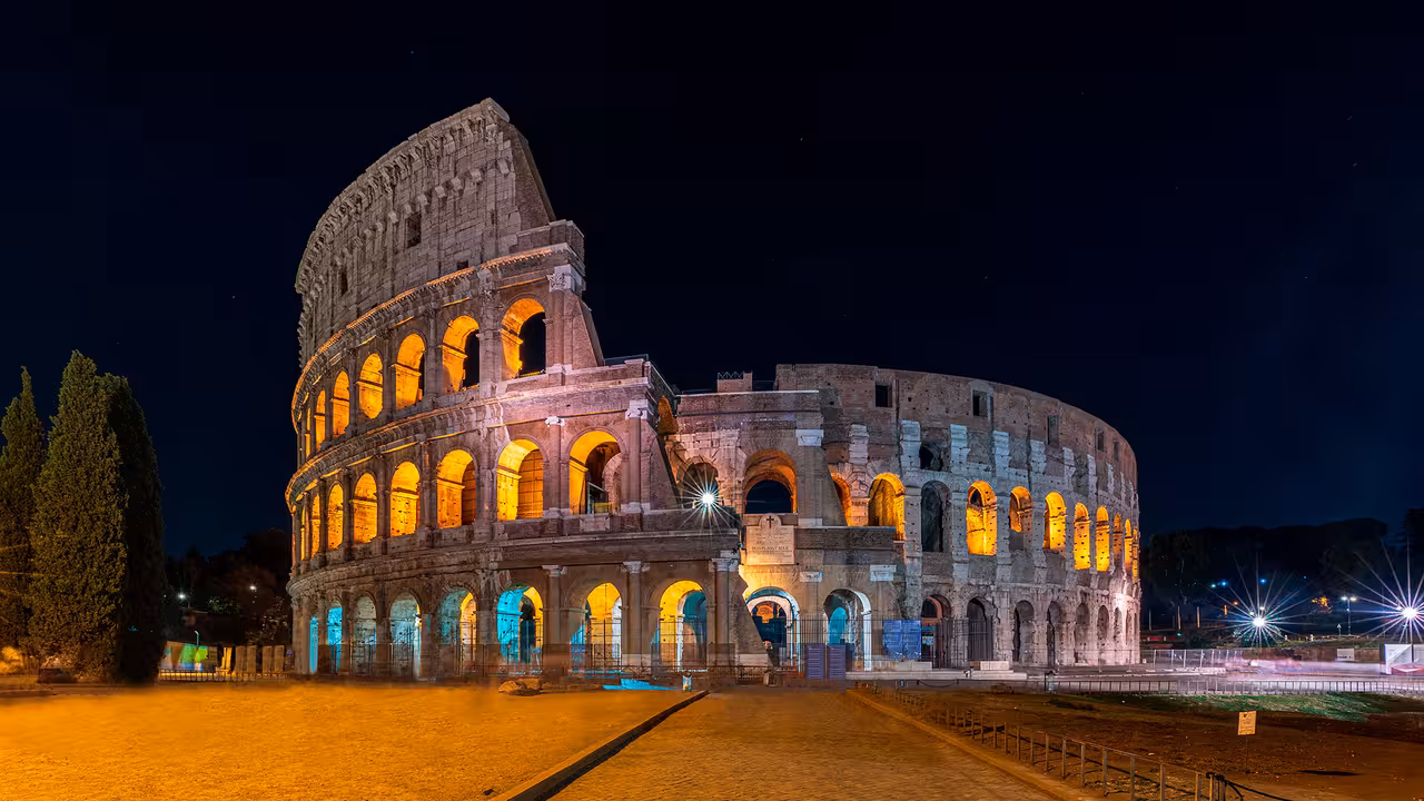 Guided Colosseum night tour in Rome with golden lights illuminating ancient arches against a clear, starry sky