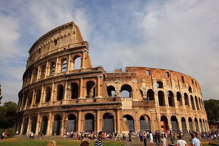 The majestic Colosseum in Rome with tourists exploring its ancient architecture under a bright blue sky.