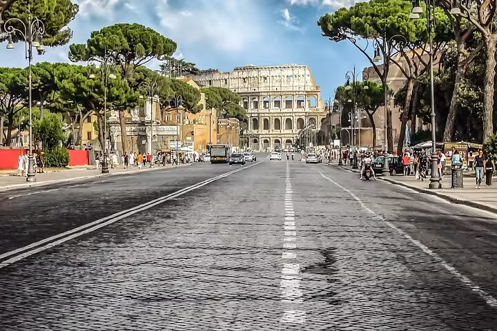 Scenic road leading to the iconic Colosseum, surrounded by lush greenery and vibrant city life in Rome.