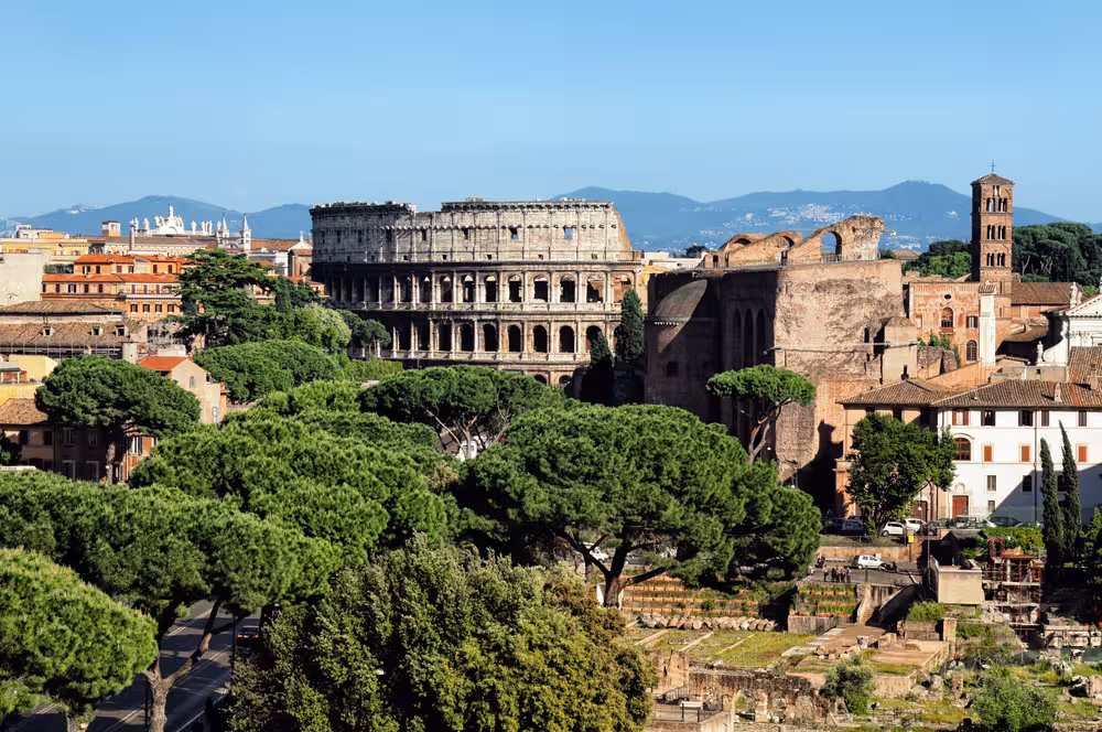 Scenic view of the Colosseum surrounded by lush greenery and ancient Roman architecture under a clear blue sky.
