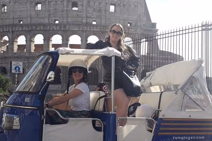 Two women on a tuk-tuk with the Colosseum in the background during a virtual tour in Rome.