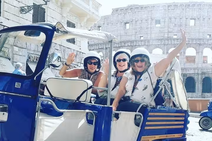 Tourists in a tuk-tuk wave excitedly with the Colosseum in the background, highlighting the Roman adventure of a virtual tour.