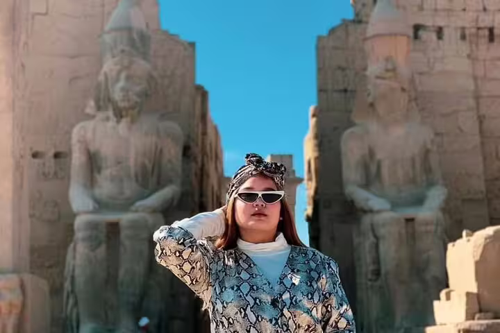 Traveler posing by the Colossi of Memnon on Luxor West Bank Nile tour, Egypt ancient statues and ruins