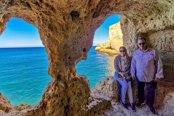 Couple exploring scenic Algar Seco caves during private boat tour from Comporta to Algarve, showcasing stunning coastal views.
