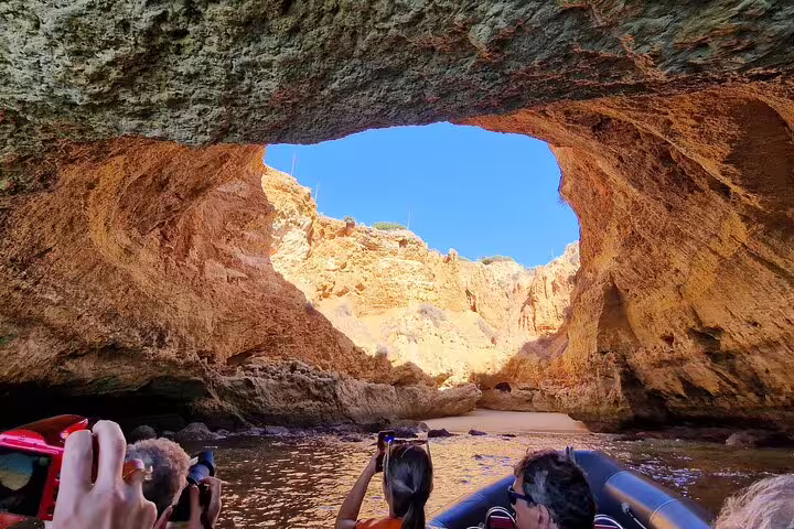 Tourists on a boat capture stunning views of the Benagil caves' natural rock formations on a Comporta to Algarve private tour.