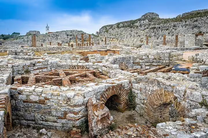 Ancient Roman ruins of Conimbriga with stone arches and columns under a clear blue sky, near the Sanctuary of Fatima.