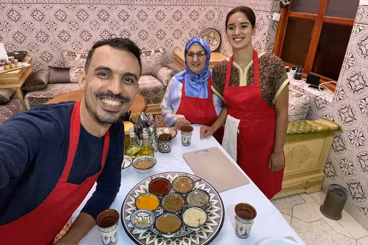 Group of three happy participants in red aprons at a cooking class, showcasing a variety of spices on a table.