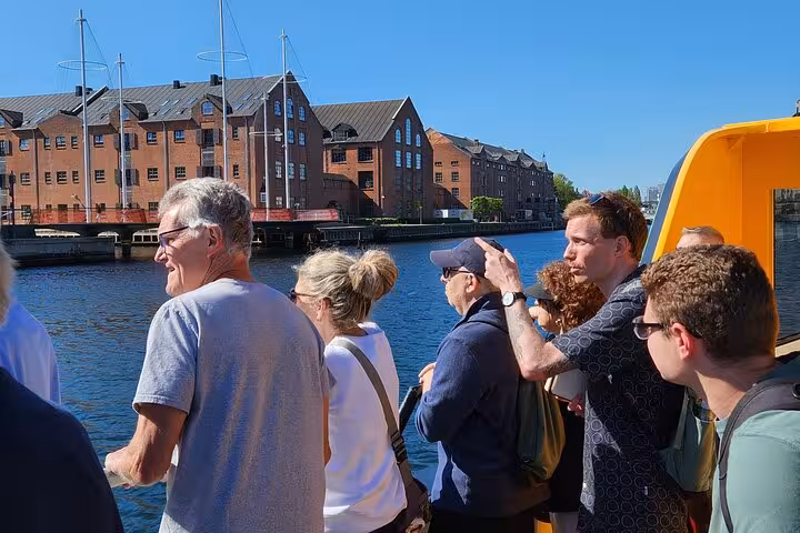 Tourists enjoy scenic views on a ferry tour of Copenhagen, with historic brick buildings along the canal.