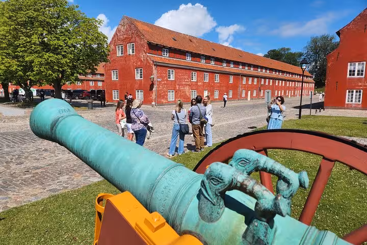 Visitors gather near a historical cannon at a red-brick fortress in Copenhagen, capturing the essence of Danish history.