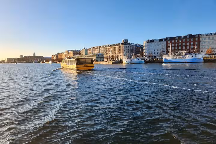 A ferry cruises through Copenhagen's waterfront, showcasing picturesque architecture and sunny skies.