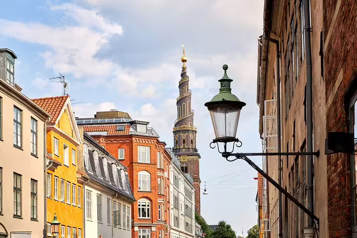 Colorful historic buildings line a street in Copenhagen with the iconic Church of Our Saviour tower in the background.