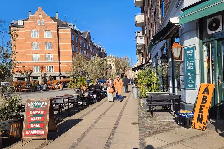 Charming Copenhagen street with outdoor cafes and people enjoying a sunny day on a walking tour.