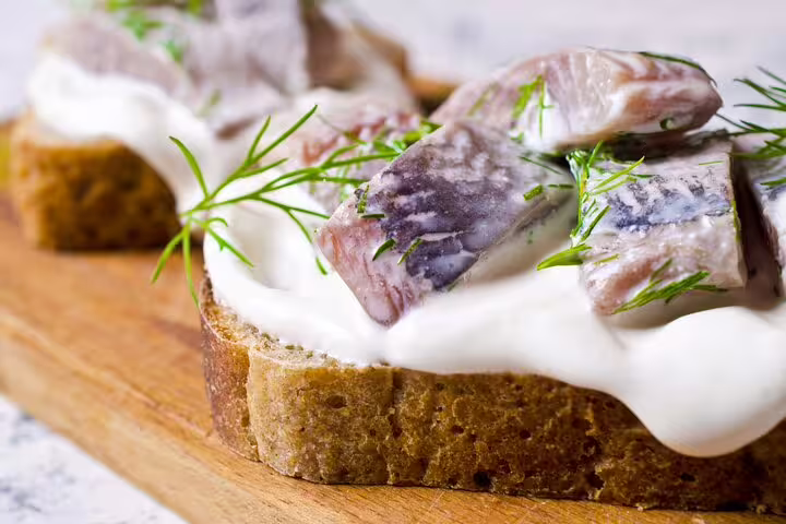 Open-faced rye sandwich with pickled herring, creamy sauce, and fresh dill, featured in the Copenhagen food tour tasting experience.