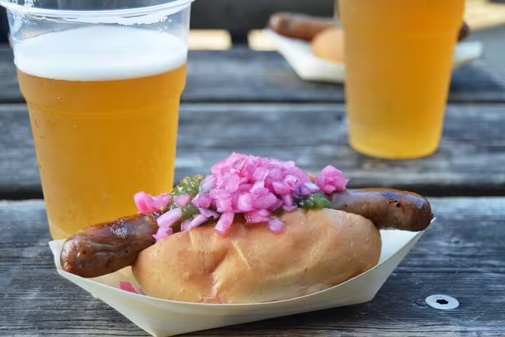Scandinavian hot dog with pickled onions and craft beer on a rustic table, featured in Copenhagen food and drink tour.