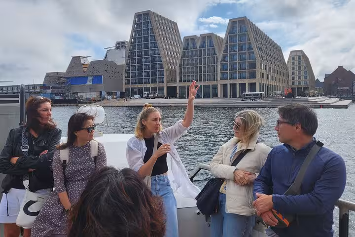 Tour guide leads a group on a ferry in Copenhagen with modern architecture in the background.