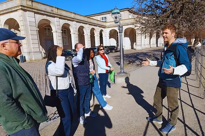 Tour guide engaging a group of tourists outside a historic building in Copenhagen under clear blue skies.