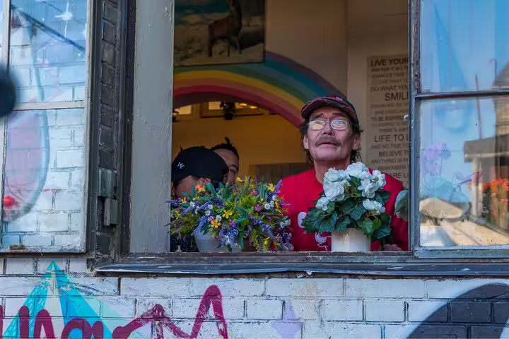 A man stands smiling at a colorful window adorned with flowers and graffiti in Copenhagen's vibrant Vesterbro district.