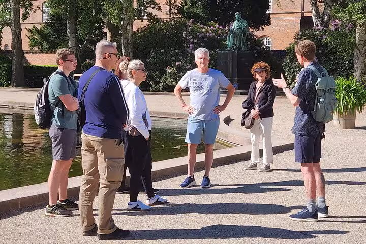 A guide leads a group tour in a picturesque Copenhagen park, with statues and vibrant flowers enhancing the experience.