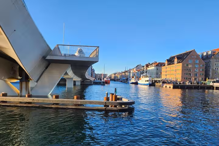 View of Copenhagen's scenic waterfront with modern bridge and colorful buildings under a clear blue sky.