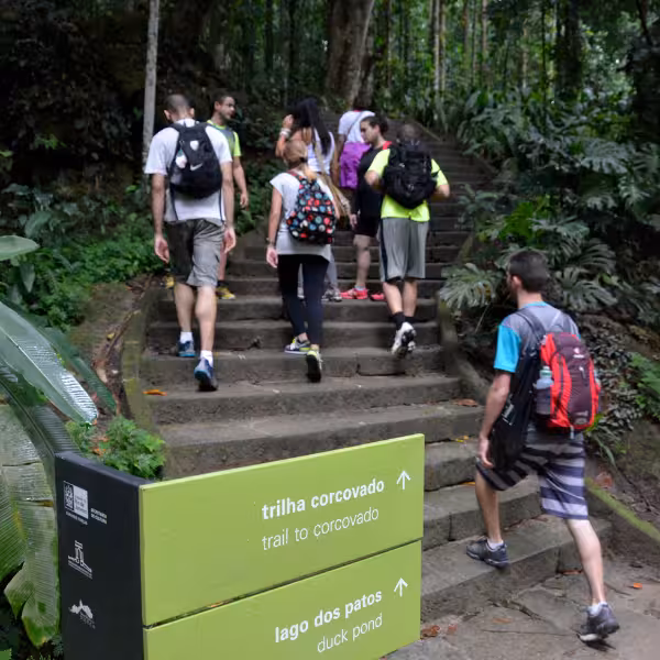 Hikers ascending the Corcovado Trail in a lush forest, sign pointing to Christ the Redeemer.