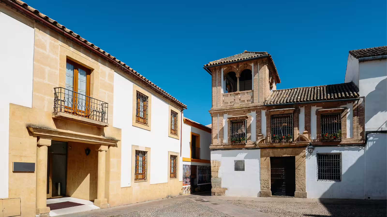 Cordoba group walking tour in the Jewish Quarter, whitewashed houses and historic plaza under blue sky