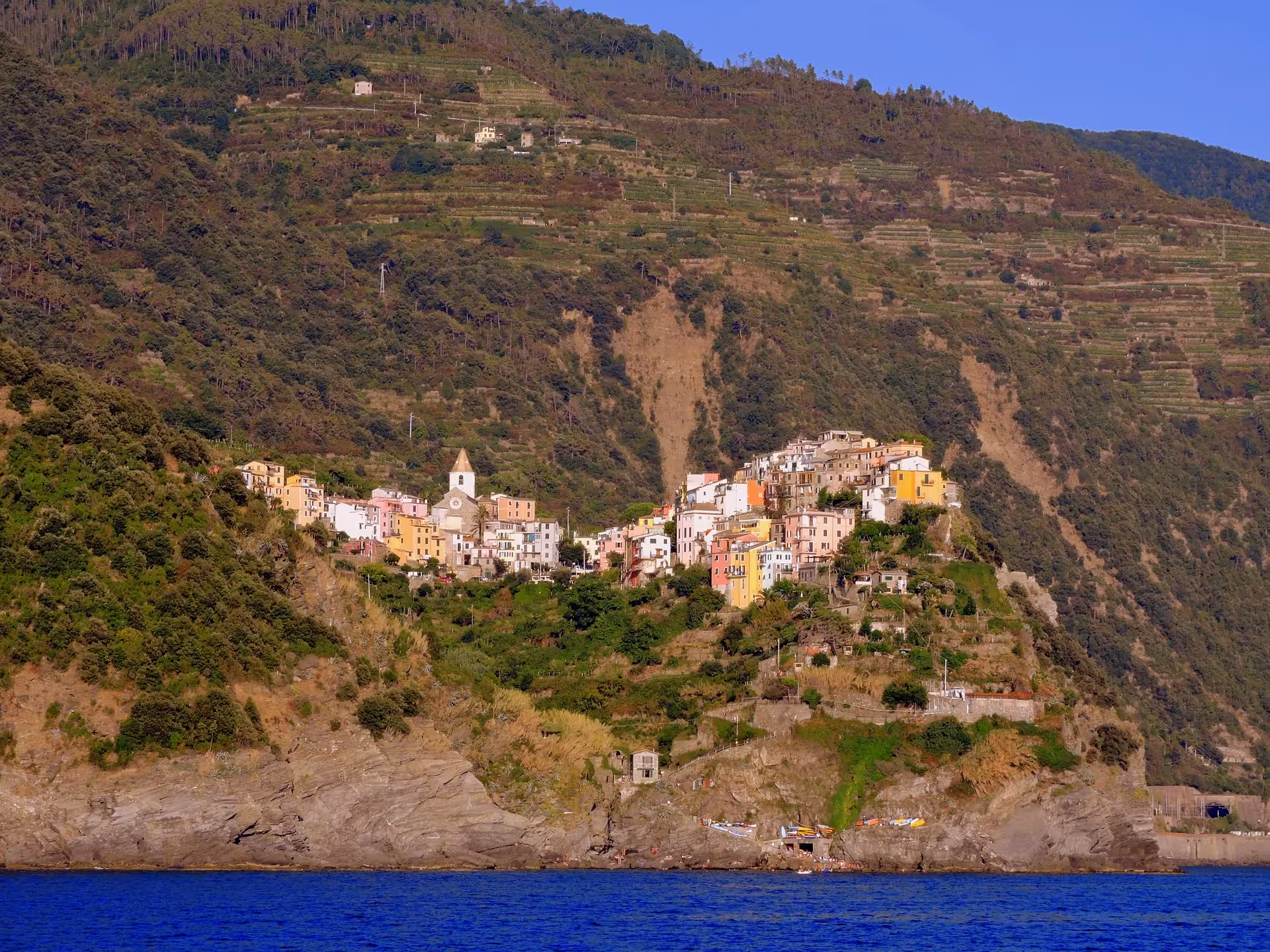 Scenic view of Corniglia village perched on a lush hillside overlooking the blue Ligurian Sea, Cinque Terre tour.
