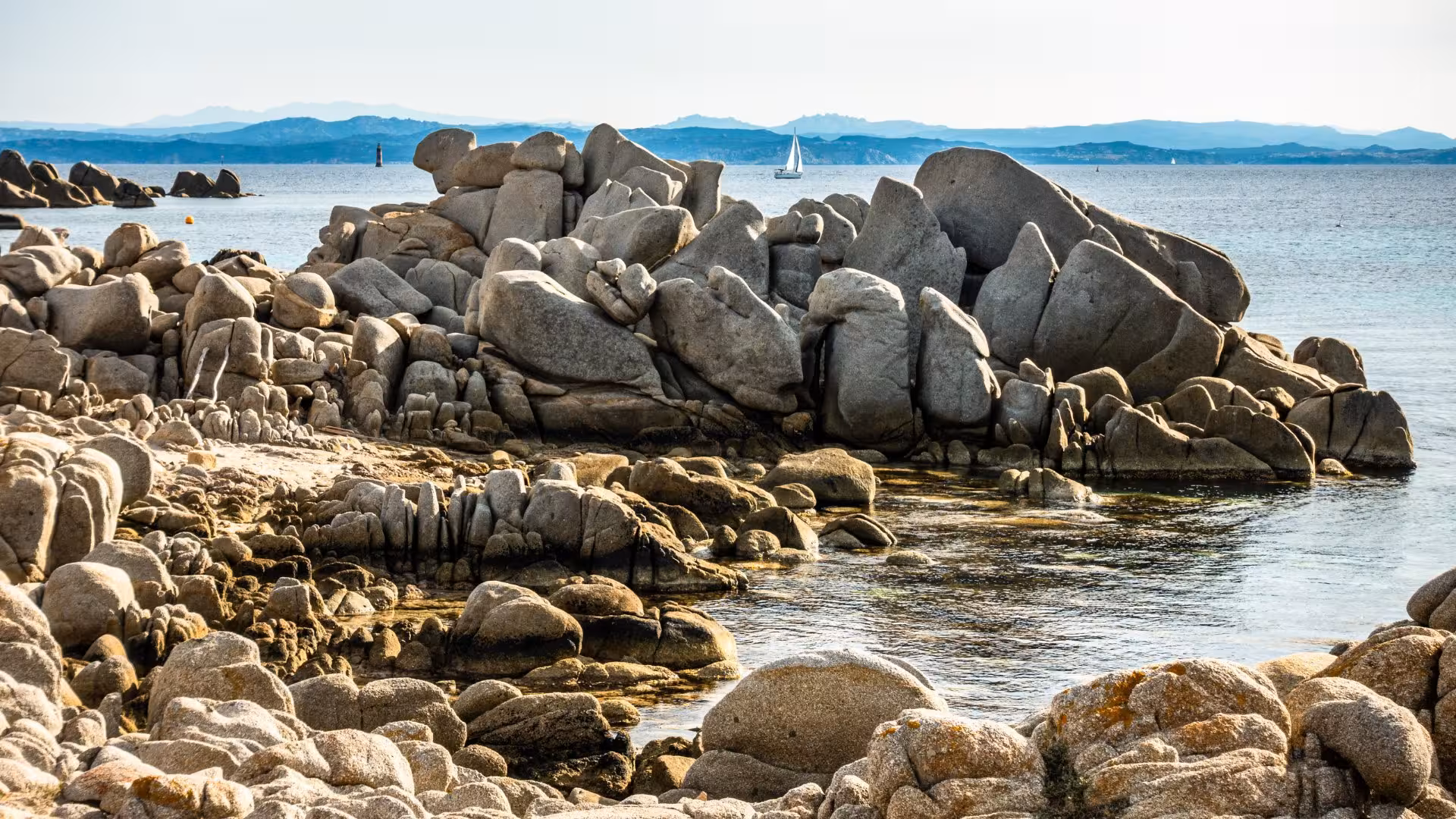 Dramatic rocky coastline of southern Corsica with a sailboat in the distance, ideal for a 4-hour RIB tour from Palau.