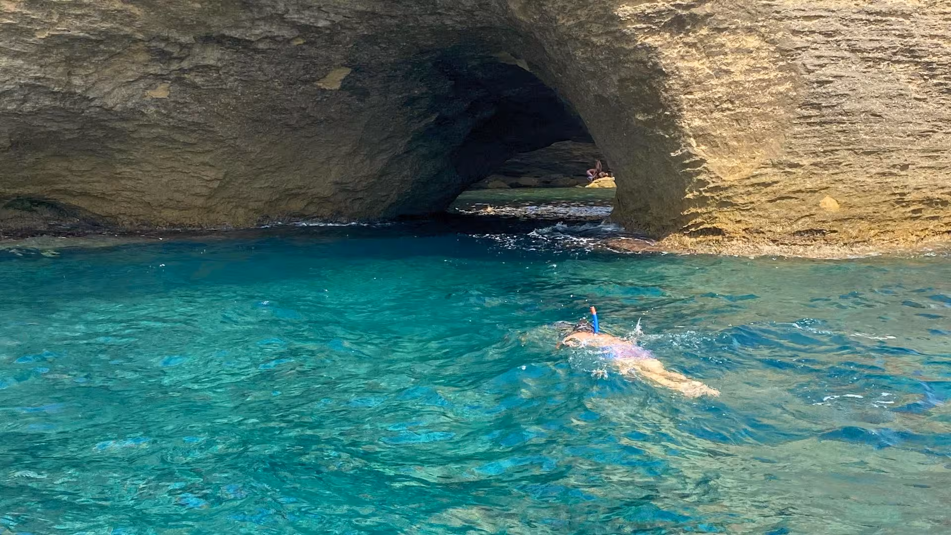A snorkeler explores the clear blue waters near a rocky arch on the southern Corsica RIB tour.
