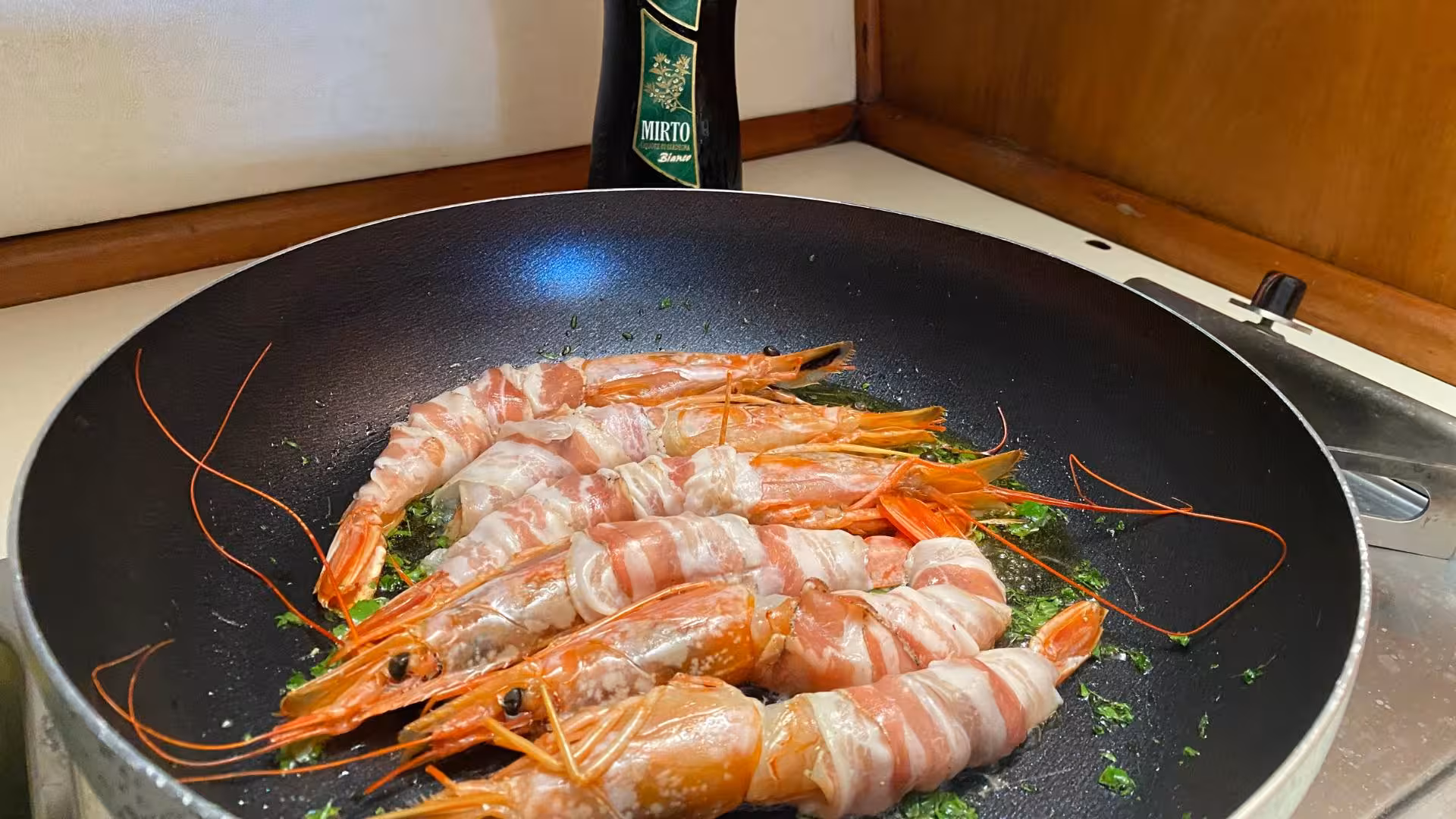 Gourmet shrimp wrapped in bacon sizzling in a pan, highlighting the culinary delights on Corsican wooden boat tours.